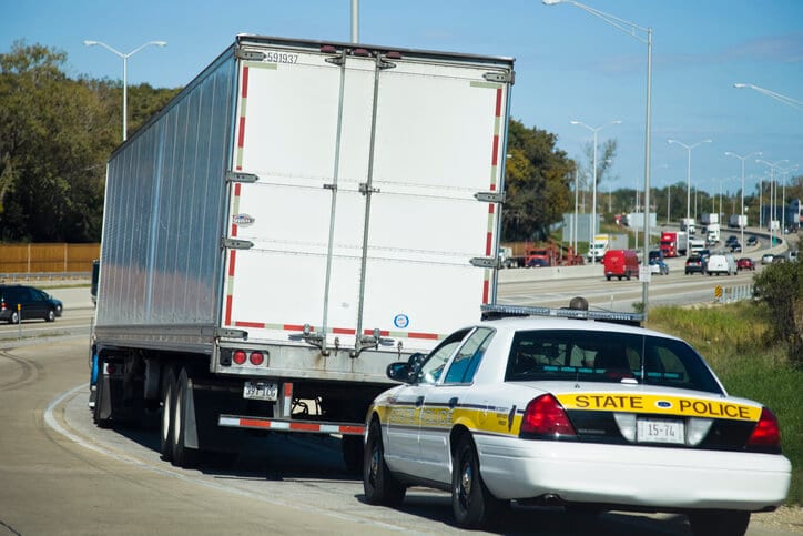 A police car sits behind a laege white truck during ELD inspection