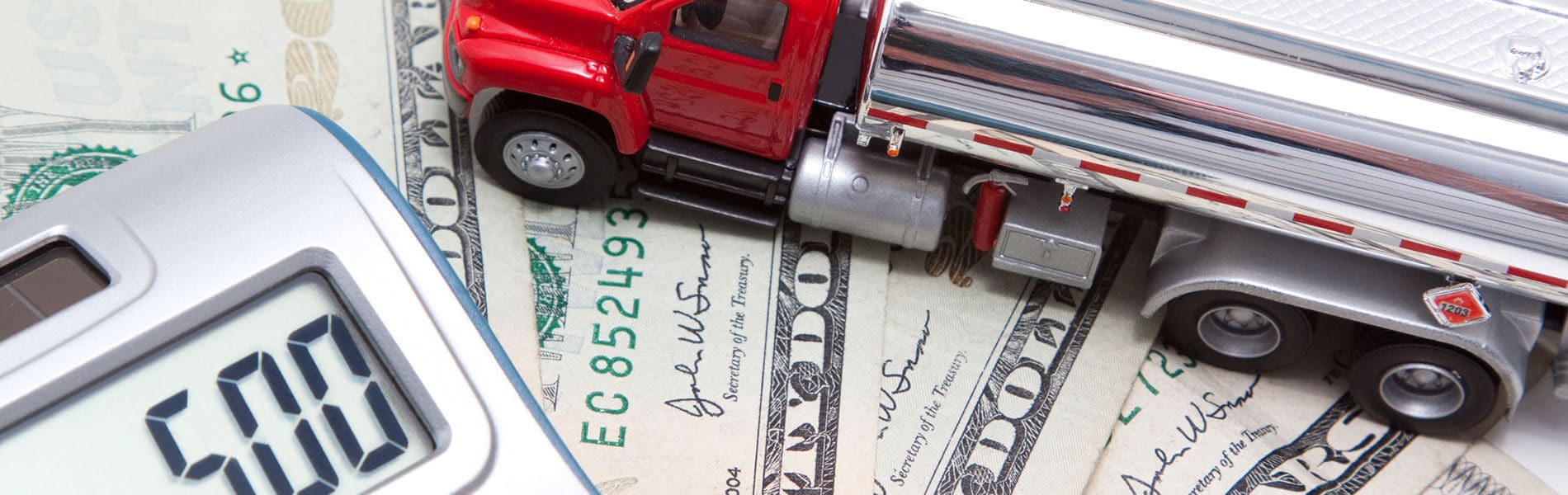 A toy truck sits on some dollars bills and a calculator