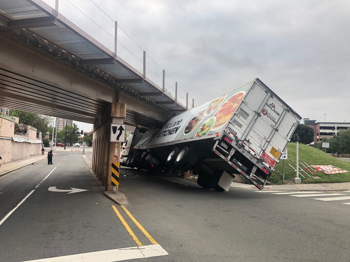 a semi truck carrying food is caught under a bridge that was too small to travel under