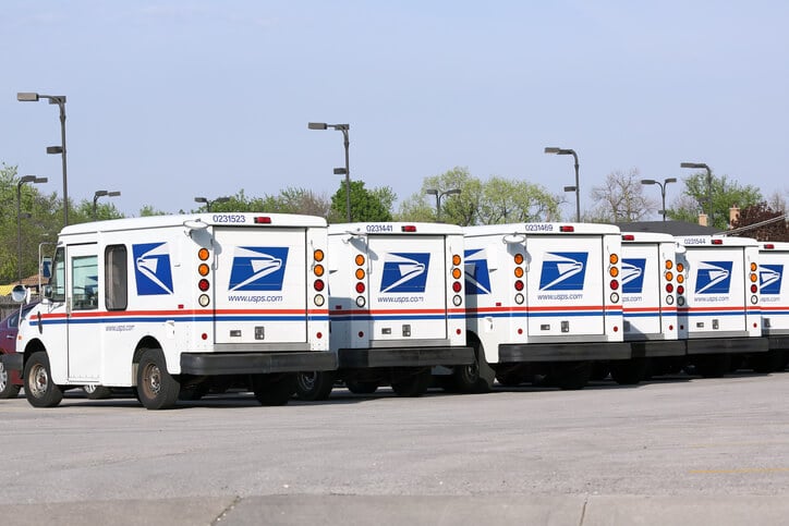 A row of government post office vehicles sit lined up in a parking lot