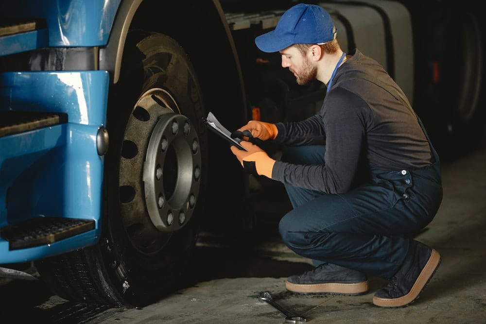 A shop worker inspects the wheels on a fleet truck. Fleet manager habits include regular maintenance.