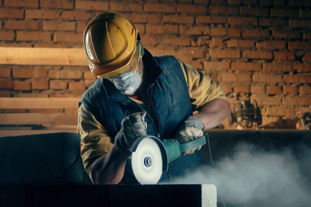 Construction working wearing a respirator while using a power tool.